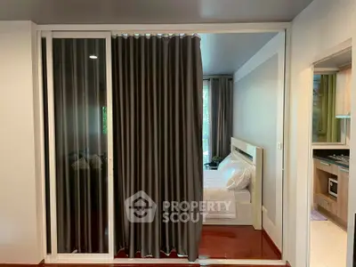 Cozy bedroom with sliding glass doors and elegant curtains, adjacent to a modern kitchen.