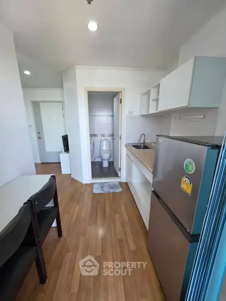 Modern compact kitchen with wooden flooring and adjacent bathroom in a cozy apartment.