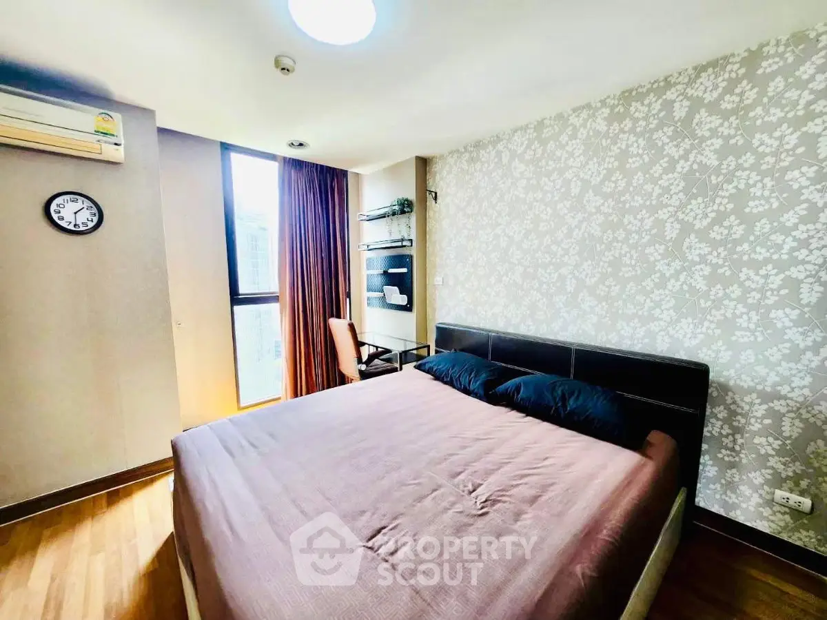 Cozy bedroom with modern decor, large window, and stylish wallpaper in a well-lit apartment.