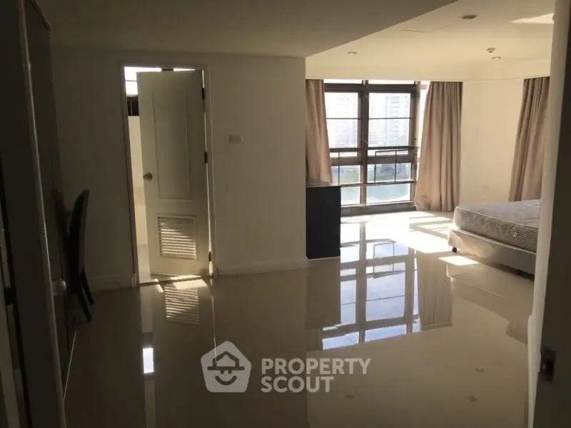 Spacious bedroom with large windows and glossy tiled floors in modern apartment.