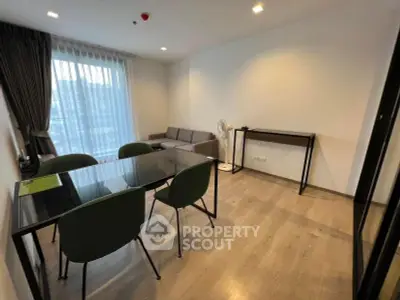 Modern living room with glass dining table and green chairs, featuring a cozy sofa and large window.