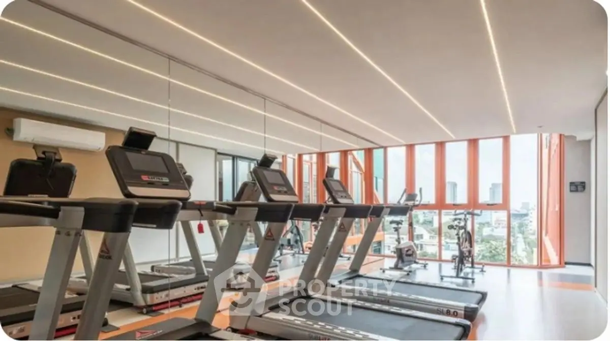 Modern gym with treadmills and large windows offering city views in a luxury apartment building.