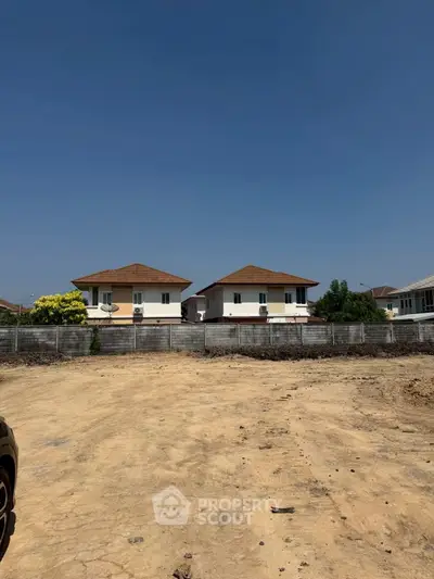 Vacant land with potential for development, surrounded by modern houses under a clear blue sky.