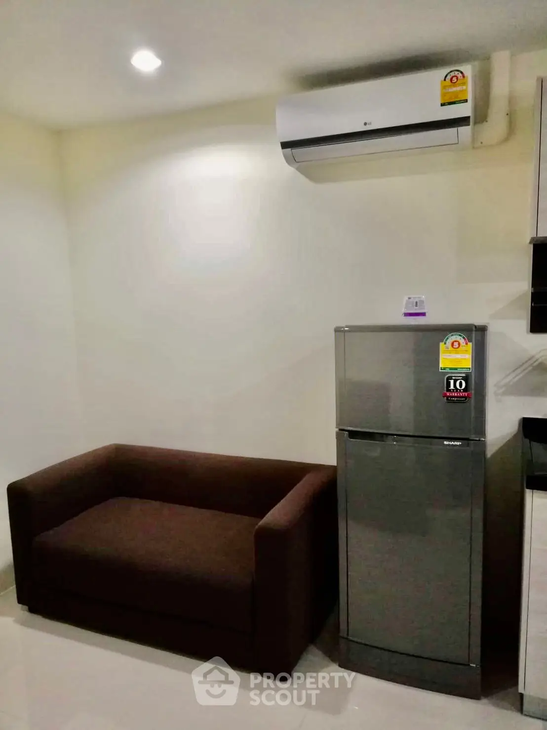 Modern apartment interior with compact sofa and sleek refrigerator under air conditioning unit.