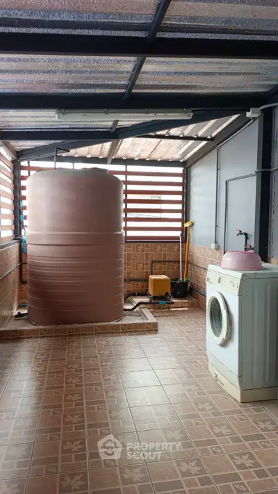 Spacious laundry area with washing machine and water tank, tiled flooring, and ample natural light.