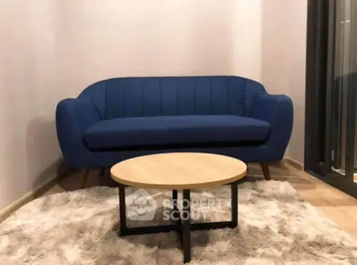 Modern living room with stylish blue sofa and round wooden coffee table on plush rug.