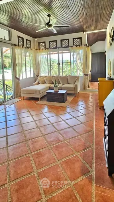 Spacious living room with large windows and elegant tile flooring, perfect for relaxation and entertaining.