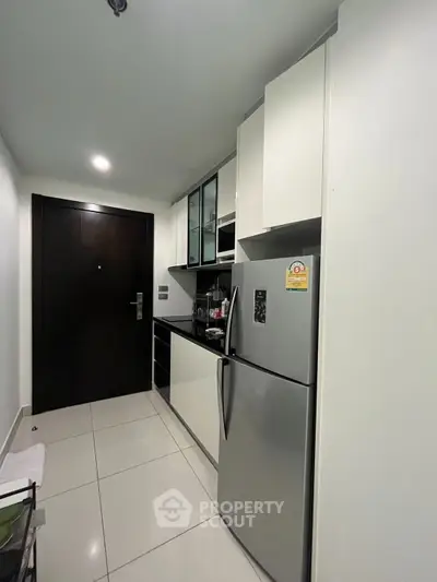 Modern kitchen with sleek cabinets and stainless steel fridge in a compact layout.