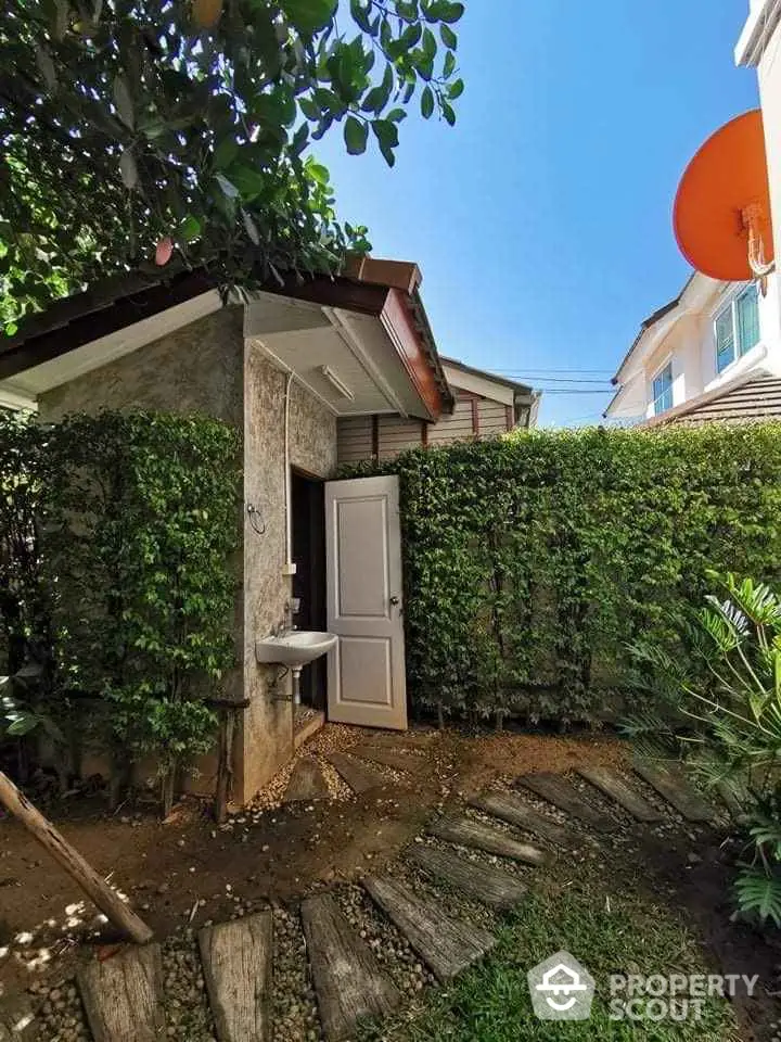 Charming garden pathway leading to a quaint outdoor shed with lush greenery and bright blue sky.