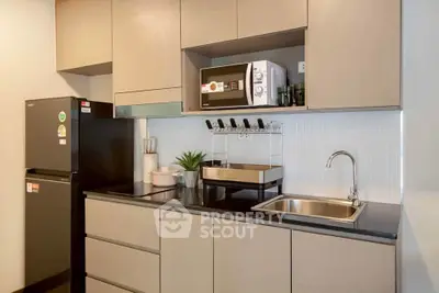 Modern kitchen with sleek cabinets, microwave, and stainless steel sink in a stylish apartment.