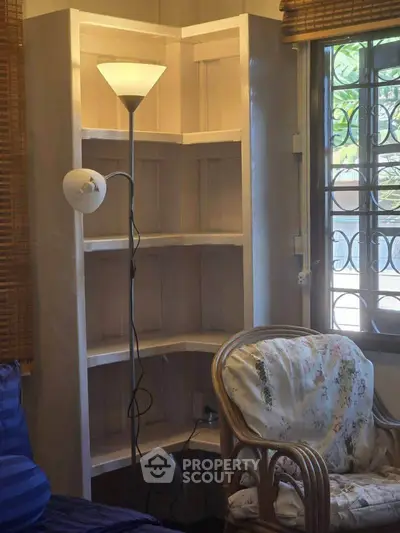 Cozy corner with a floor lamp, wicker chair, and wooden shelves by a window with blinds.