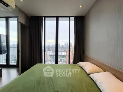 Modern bedroom with panoramic city view from floor-to-ceiling windows, featuring a cozy green bedspread.