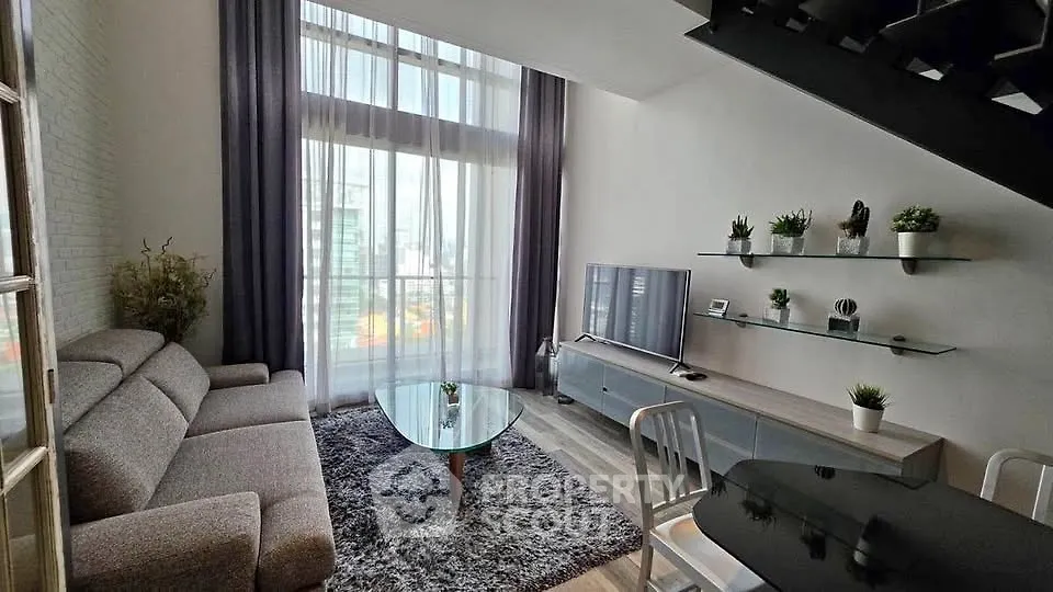Modern living room with high ceiling, large windows, and stylish decor in urban apartment.