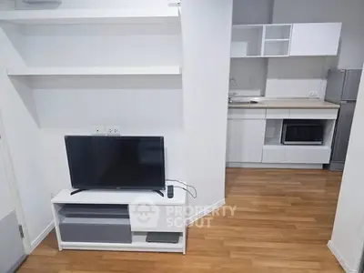 Modern open-layout living room with sleek kitchen and wooden flooring, featuring a TV stand and contemporary appliances.