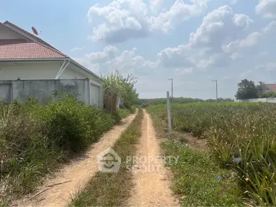 Scenic rural property with dirt road and lush greenery under a bright blue sky.