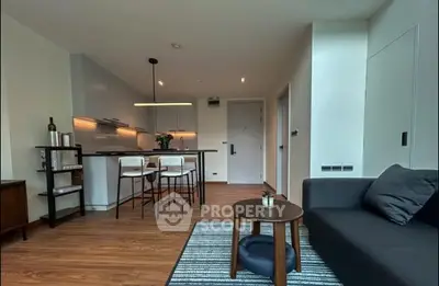 Modern living room with open kitchen, stylish furniture, and warm lighting.