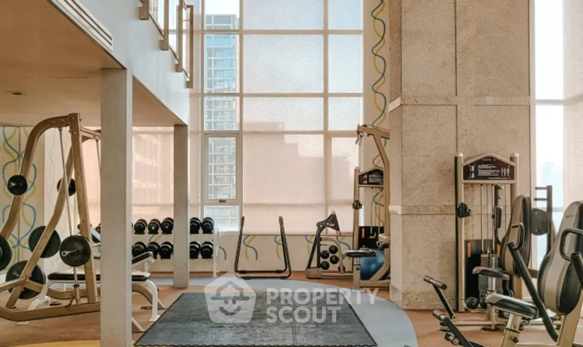 Spacious modern gym with large windows and fitness equipment in luxury building.
