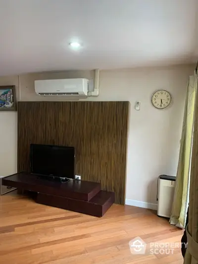 Modern living room with wooden flooring, wall-mounted TV, and air conditioning unit.