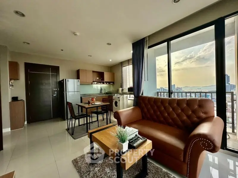 Modern open-plan living room with kitchen, featuring leather sofa and city view balcony.