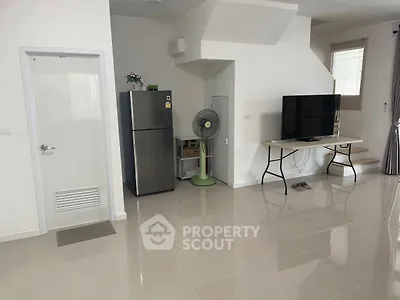 Spacious modern living room with sleek tiled flooring, featuring a large TV and refrigerator, ideal for contemporary living.