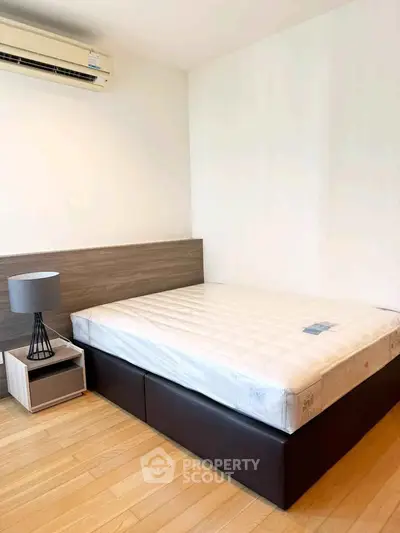 Modern bedroom with wooden flooring and air conditioning, featuring a stylish bed and nightstand.