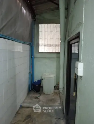 Narrow utility area with tiled walls and a window, ideal for storage or laundry setup.
