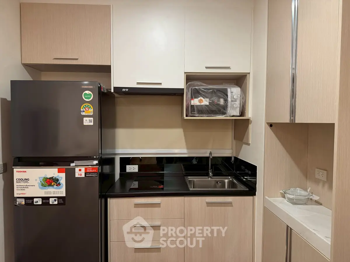 Modern kitchen with sleek cabinetry, stainless steel fridge, and built-in microwave in a compact layout.