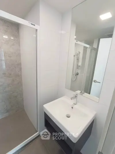 Modern bathroom with sleek sink and glass shower enclosure in contemporary apartment.