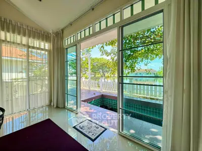 Spacious living room with large windows overlooking a serene pool and garden view.