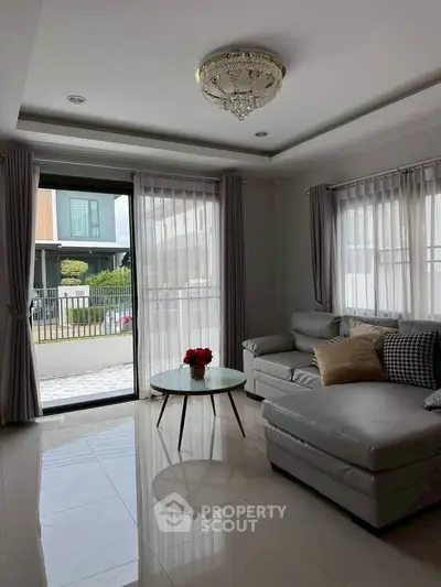 Elegant living room with modern sofa and chandelier, featuring large windows and natural light.