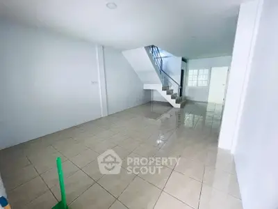 Spacious open-plan living area with tiled flooring and modern staircase in a bright home.