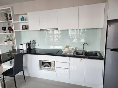 Modern kitchen with sleek white cabinets and black countertop, featuring built-in microwave and stainless steel sink.