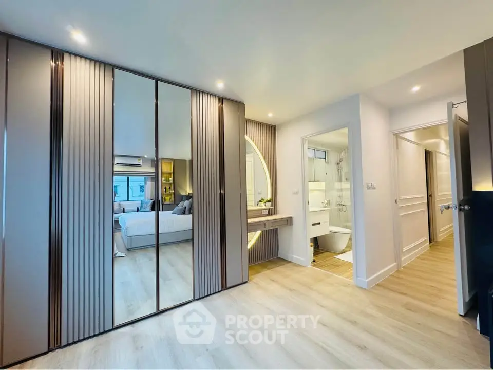 Modern bedroom with mirrored wardrobe and ensuite bathroom in luxury apartment.
