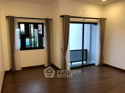 Spacious room with large windows and balcony access, featuring elegant curtains and wooden flooring.