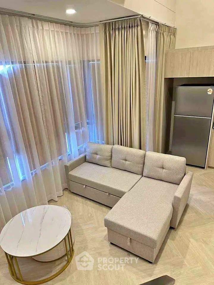 Modern living room with stylish L-shaped sofa and elegant curtains, featuring a sleek marble coffee table and a stainless steel fridge.
