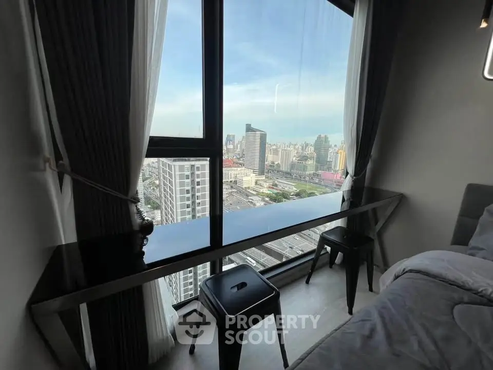 Modern bedroom with stunning city view from large window, featuring sleek black desk and stools.
