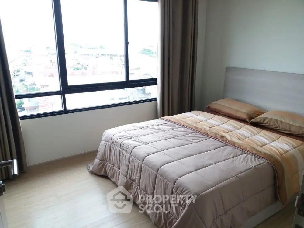 Cozy bedroom with large window offering stunning city views and natural light.