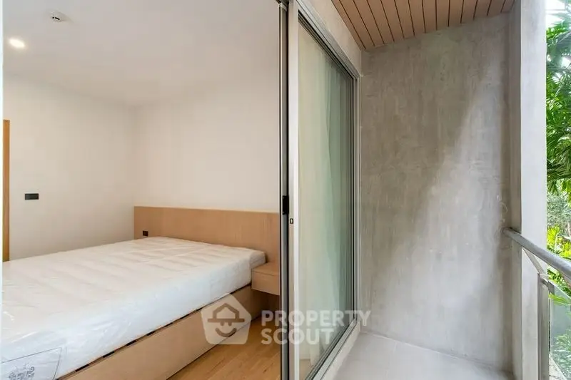 Modern bedroom with sliding glass door to a cozy balcony, featuring minimalist design and natural light.