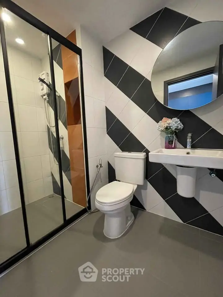 Modern bathroom with stylish black and white tiles, round mirror, and glass shower enclosure.