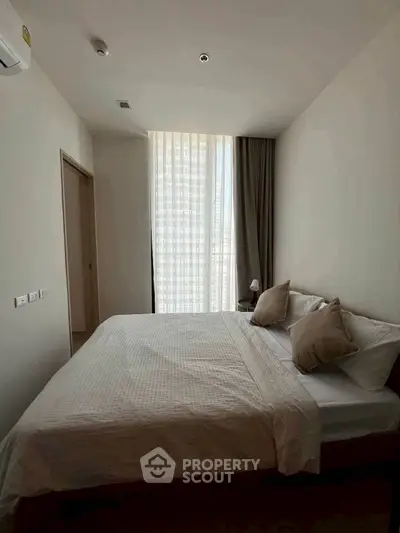 Cozy bedroom with modern decor and natural light through large window.
