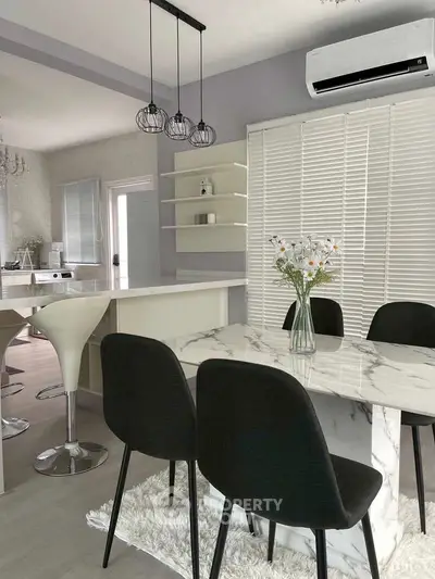 Modern kitchen with marble dining table and sleek black chairs, featuring open layout and stylish lighting.