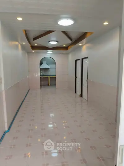 Spacious tiled hallway leading to a modern kitchen with archway and recessed lighting.