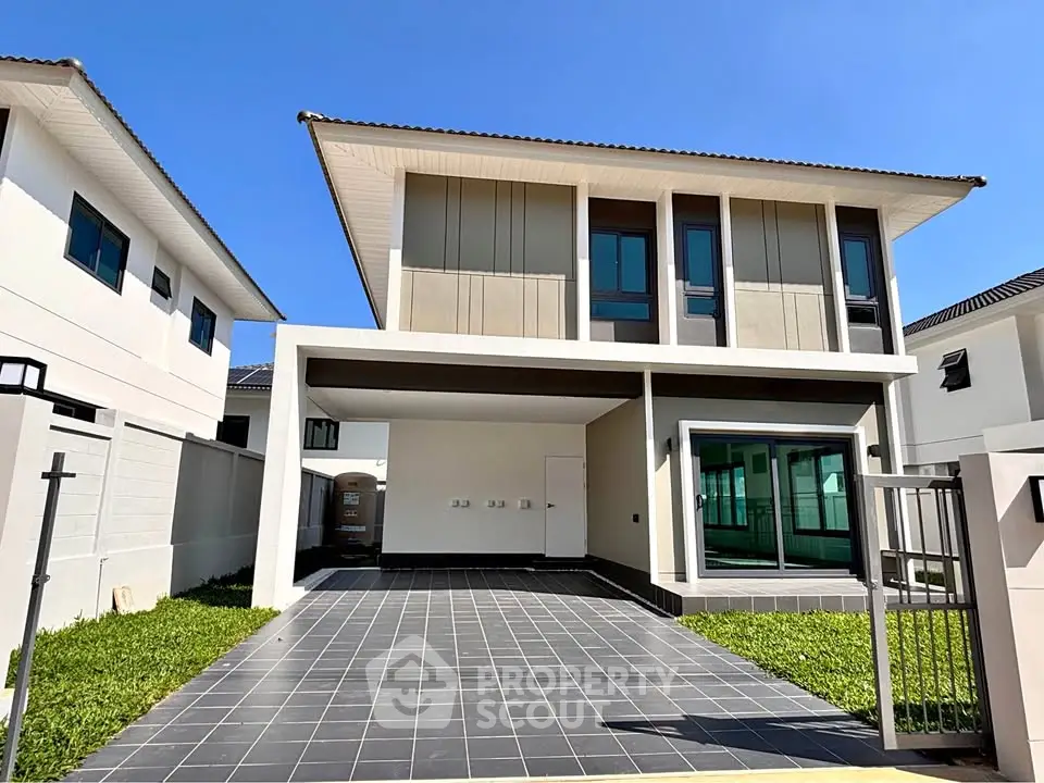 Modern two-story house with sleek design and spacious driveway under clear blue sky.