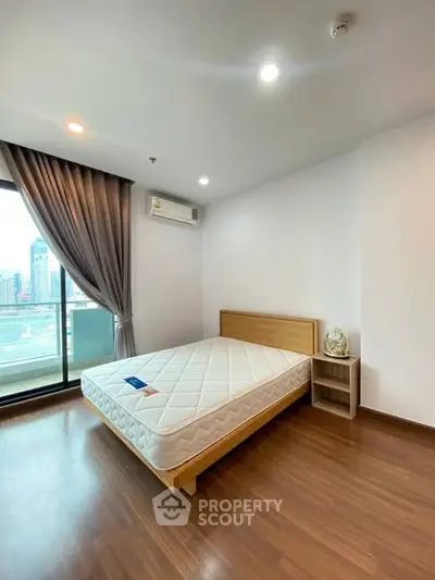 Spacious bedroom with city view and balcony access in modern apartment.