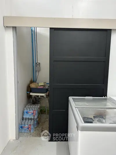 Storage area with sliding door and freezer, featuring bottled water and cleaning supplies.