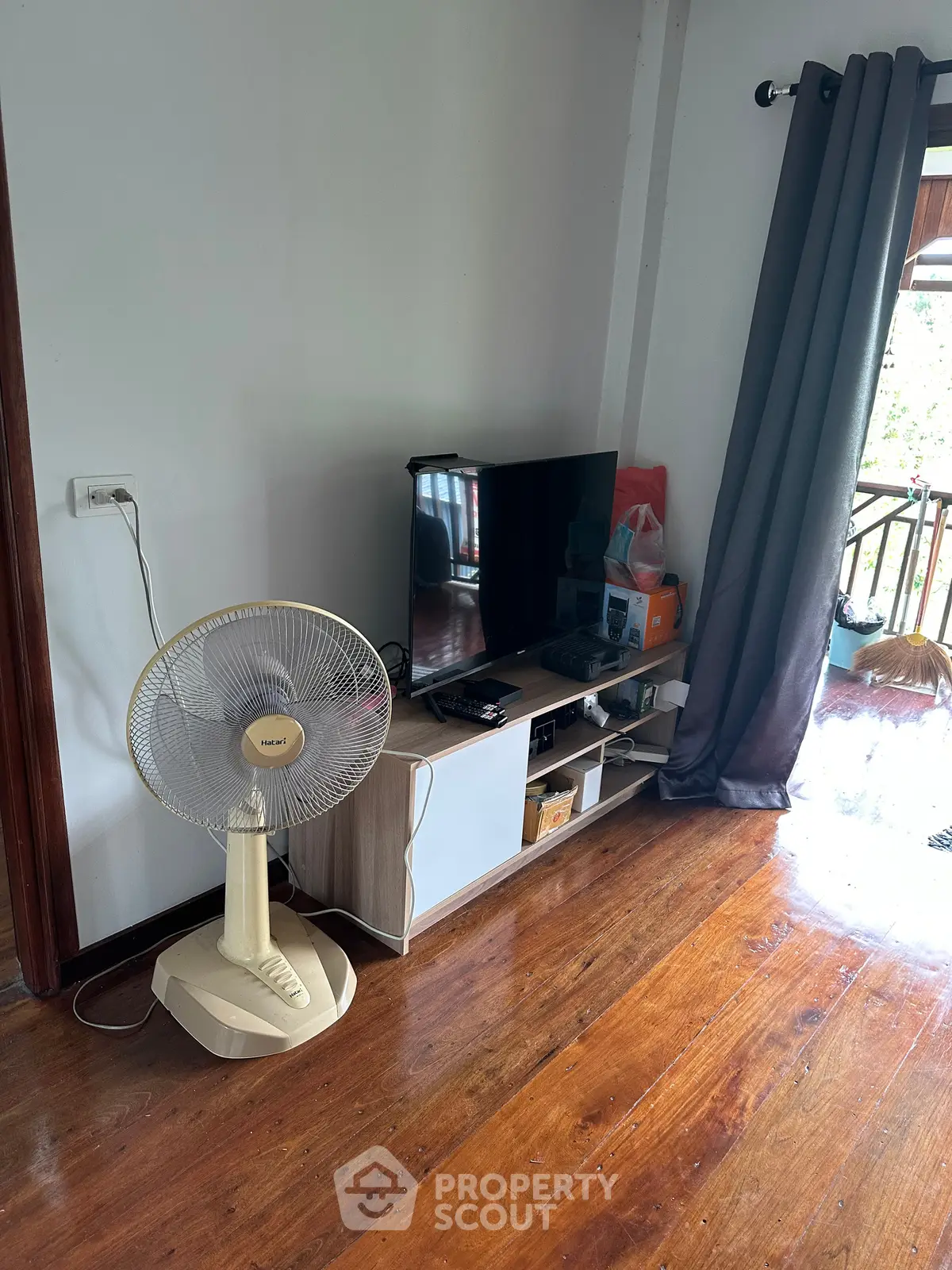Cozy living room with wooden floors, TV stand, and balcony view, perfect for relaxation.