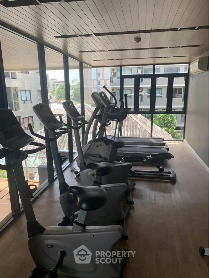 Modern gym with exercise equipment and large windows offering city views.