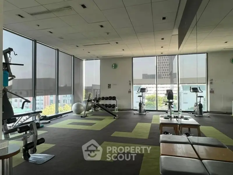 Spacious modern gym with large windows and fitness equipment in a high-rise building.