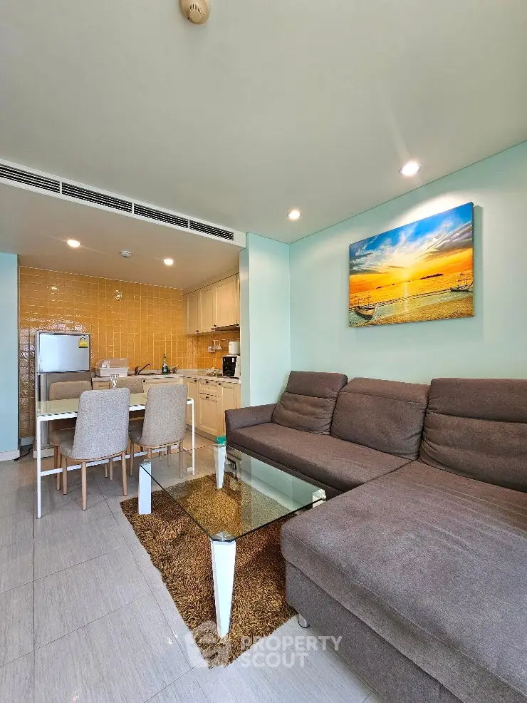 Modern living room with cozy sofa, glass coffee table, and open kitchen layout.