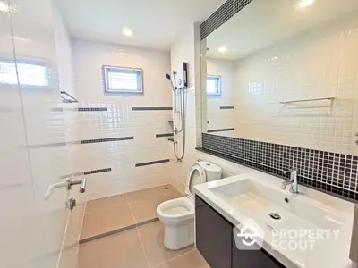 Spacious modern bathroom with sleek white tiles, large mirror, and contemporary fixtures, offering a serene and clean atmosphere.